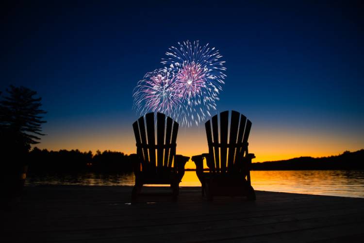 2 Adirondack chairs at beach with fireworks in the background